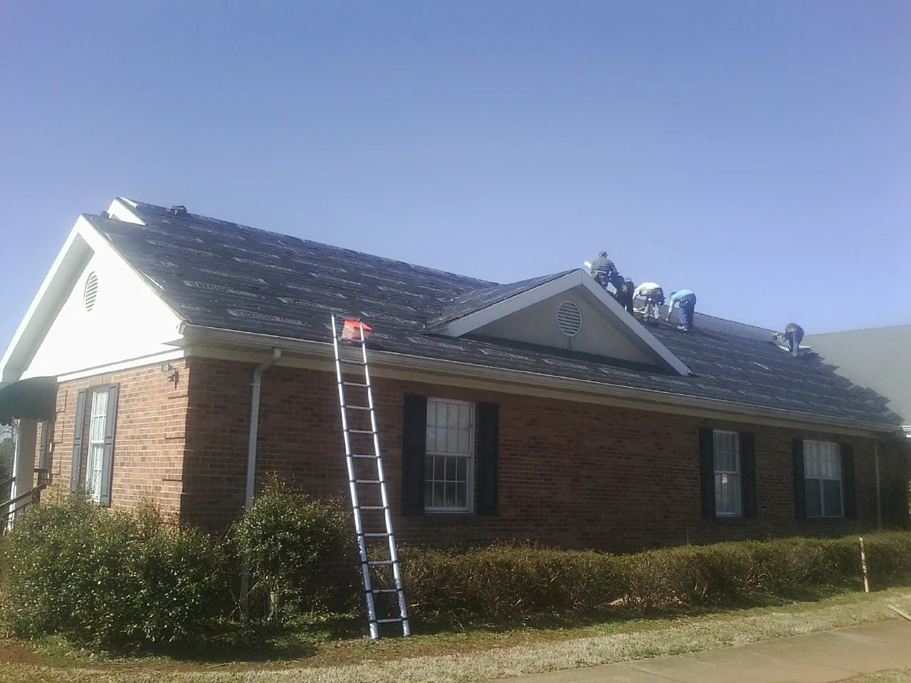 Crew tearing shingles off a brick ranch roof with a ladder set — Metal Roof Repair work by our crew in Ada
