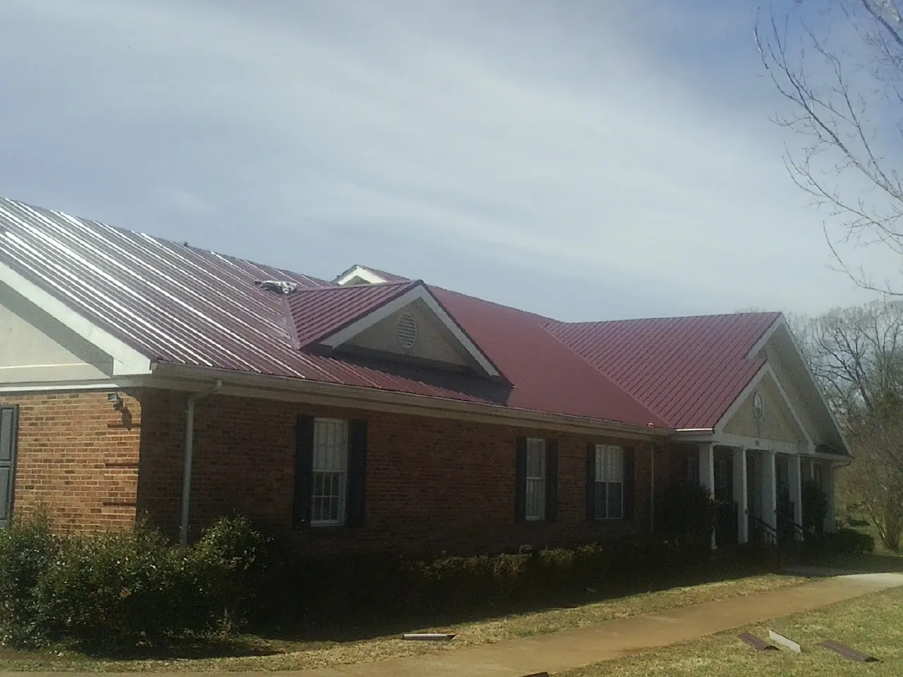 Red metal roof with gabled entries on a long brick building, from a Hail Damage Roof Repair job in Ada