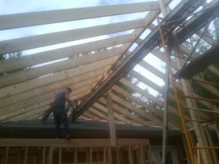 Rafters going up over a new addition with a worker on the wall in Ada