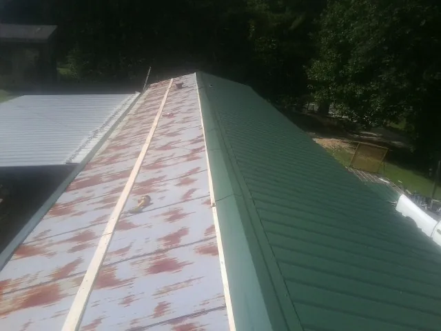 Old rusted panels beside newly installed green metal roofing — Wind Damage Roof Repair by Roofing Brothers in Ada