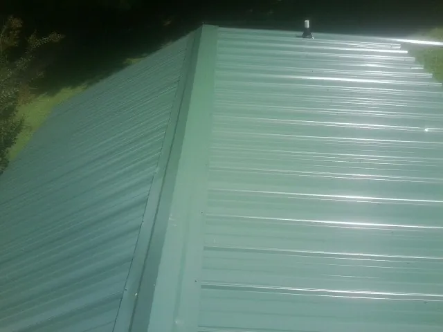 New green metal panels meeting at the ridge of a roof — Flat Roof Repair work by our crew in Ada