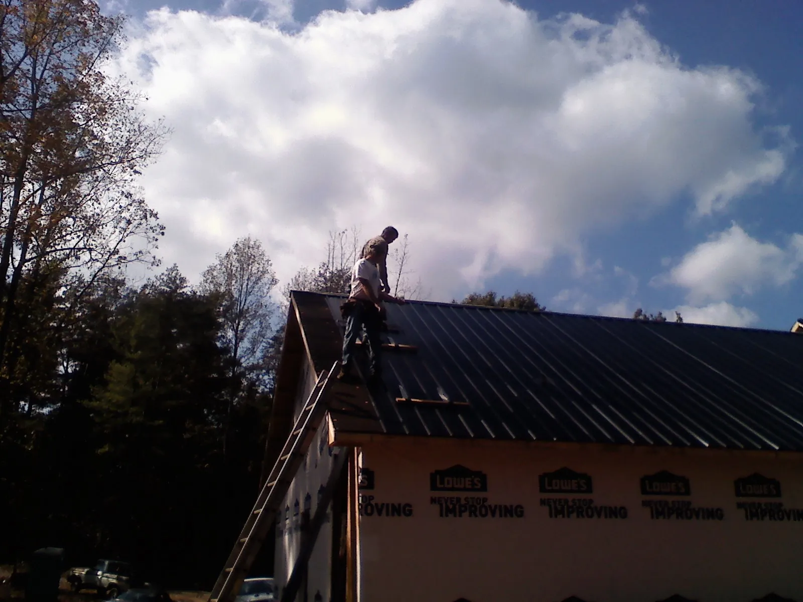 Roofer fastening dark metal panels high against a cloudy sky, from a Roof Inspection job in Ada
