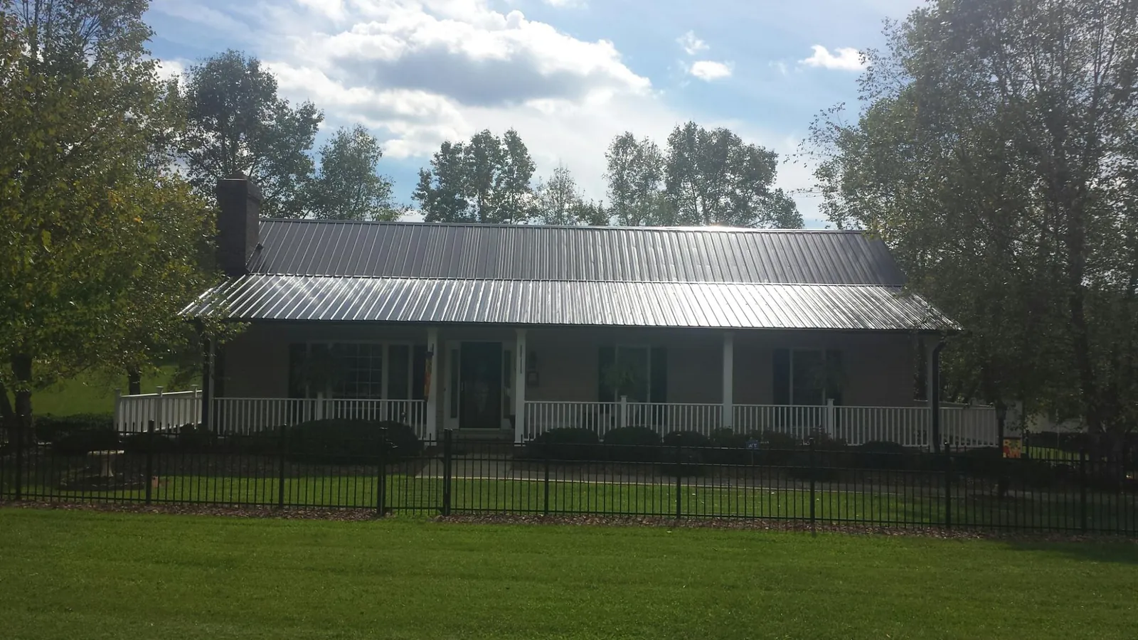 Gray metal roof on a brick ranch with a full width front porch — Gutter Guard Installation work by our crew in Ada