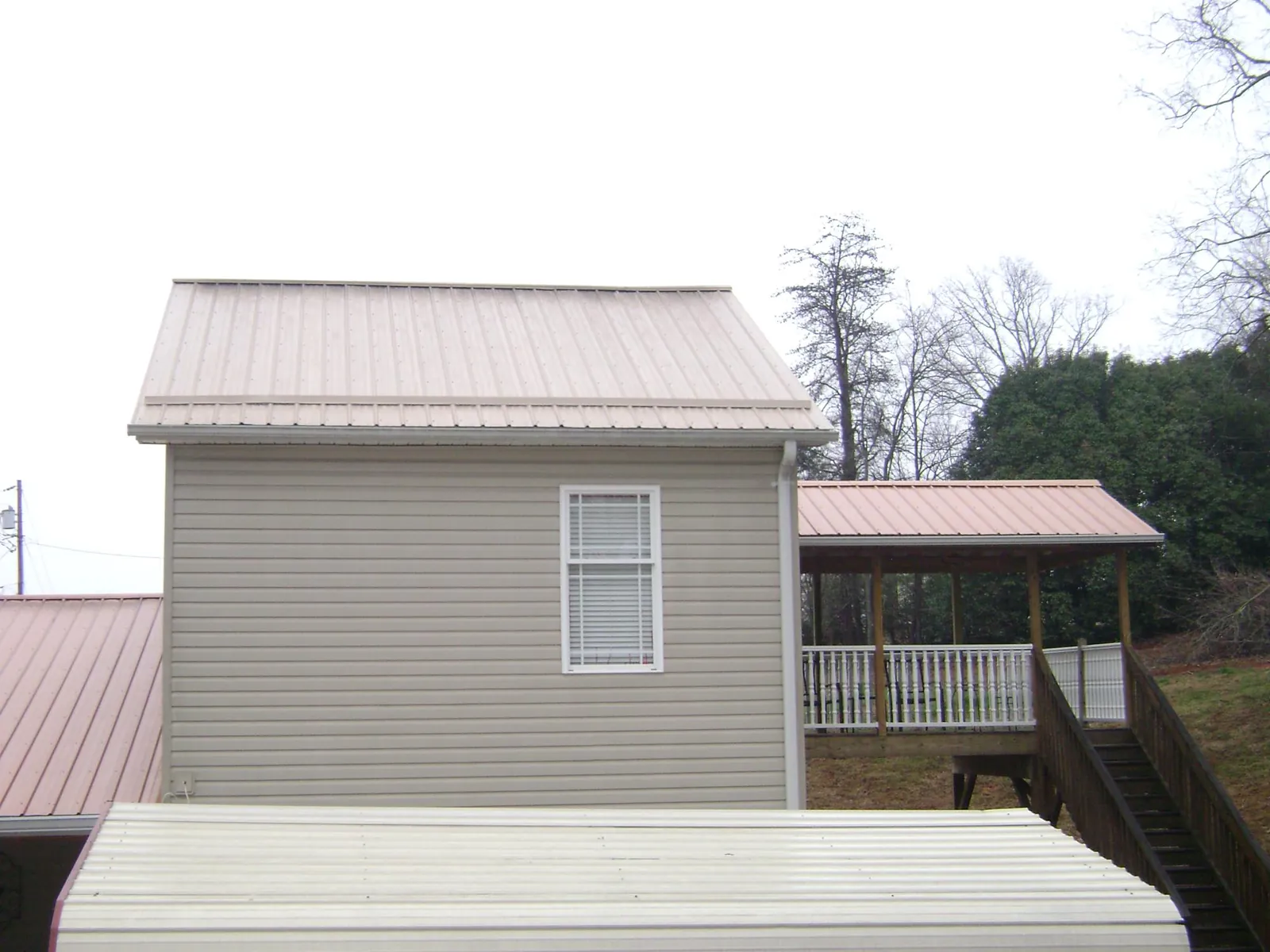 Tan metal roofs on a two story addition and attached porch, from a Roof Replacement job in Ada